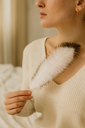 Straußenfeder weiß — Frau hält die Feder vor einem hellen Strickpullover