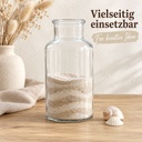 Apothekerflasche aus klarem Glas im Vintage-Look zur Hälfte mit hellem Sand geschichtet, daneben zwei Muscheln