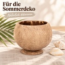 Becher aus echter Kokosnussschale mit angesetztem Standfuß auf dem sommerlich gedeckten Tisch neben Palmenblatt und Muscheln